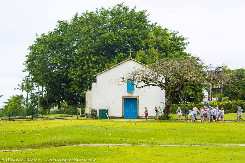 Imagem de visitantes ao lado de uma pequena igreja.